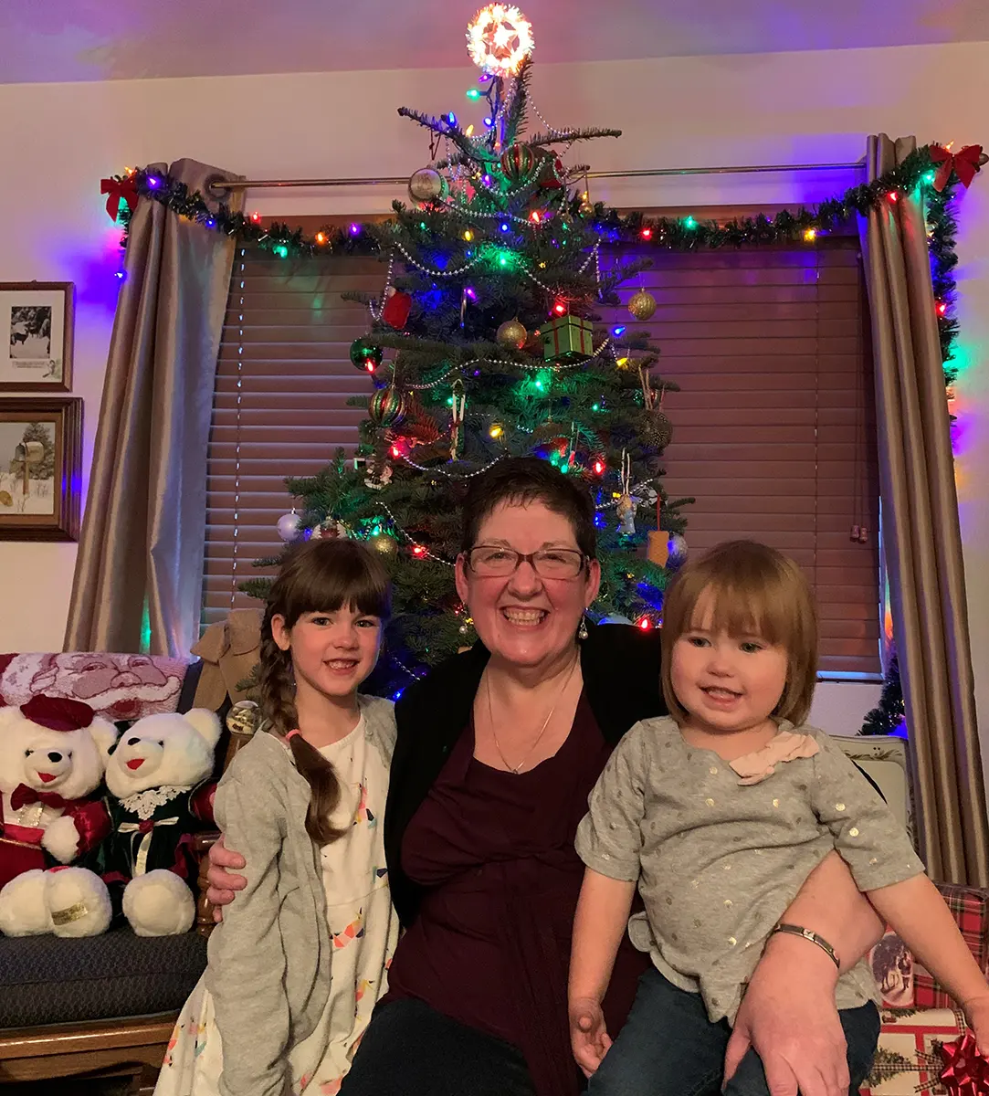 photo of a grandmother and two granddaughters sitting in front of a Christmas tree