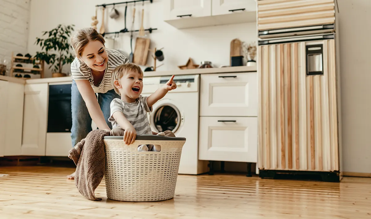 mother pushing son in a laundry basket in a kitchen
